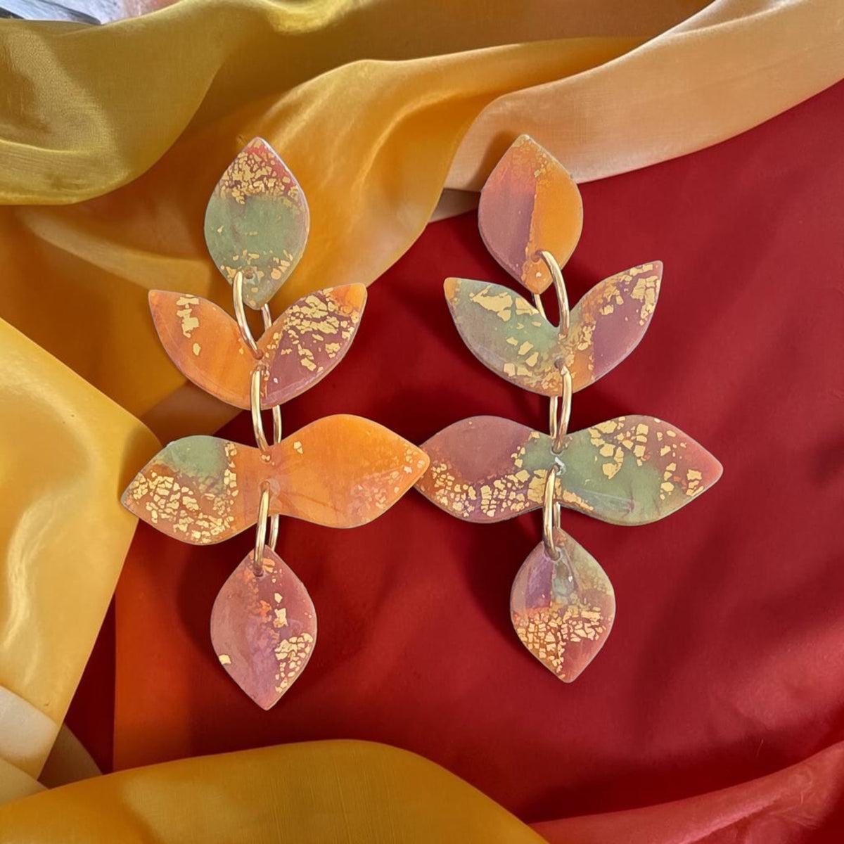 Tiered leaf dangle earrings in orange, muted green, and mauve with gold-colored flecks and connecting rings