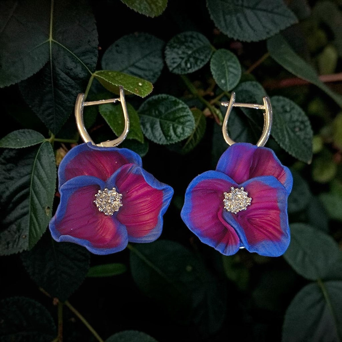 Magenta polymer clay flower earrings with blue-edged petals, sparkling silver-tone centers, and silver-tone hoops